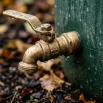 Ultra close-up macro of heavy-duty brass spigot valve on green rain barrel in autumn light